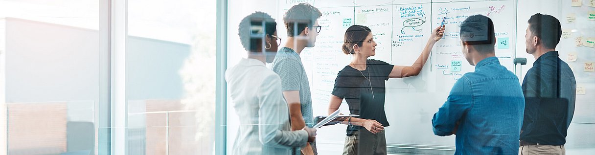 Teammeeting in einem modernen Büro: Mitarbeitende analysieren Aufgaben auf einem Whiteboard in einem agilen Arbeitsumfeld mit Fokus auf Projektplanung und Zusammenarbeit.